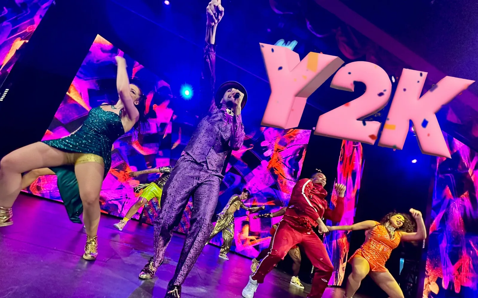 A vibrant stage performance with four dancers in colorful outfits under large illuminated "Y2K" letters.