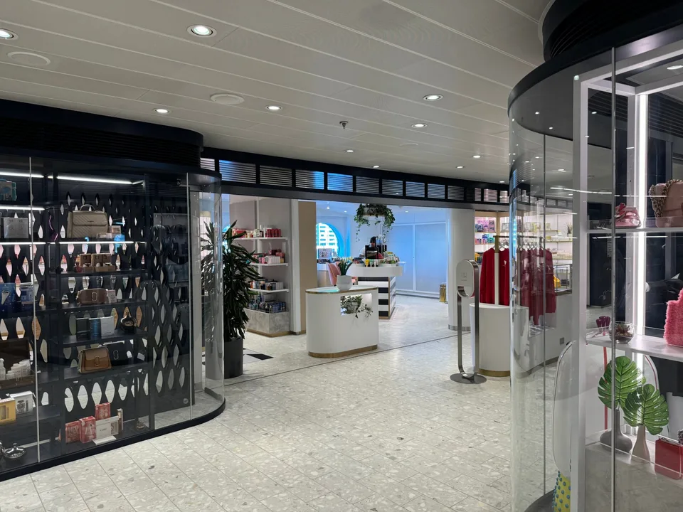 Interior view of a modern onboard shop displaying various items including plants, bags, and apparel with a white and black color scheme.