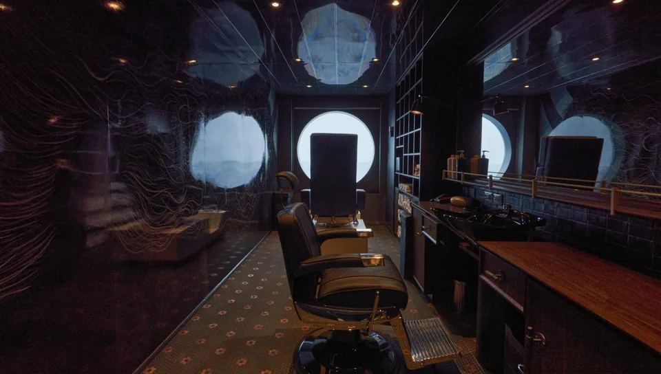Interior of a compact grooming or barber station with a chair, large round mirror, and dark reflective walls.