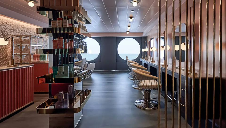 Interior of a salon area with chairs and haircare products displayed, featuring large round windows with a view of the sea.