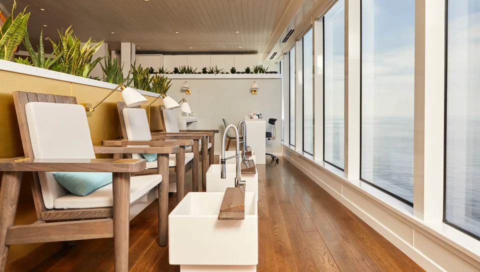 Interior view of a cruise ship or ferry passageway with wooden floors and large windows showing the ocean.