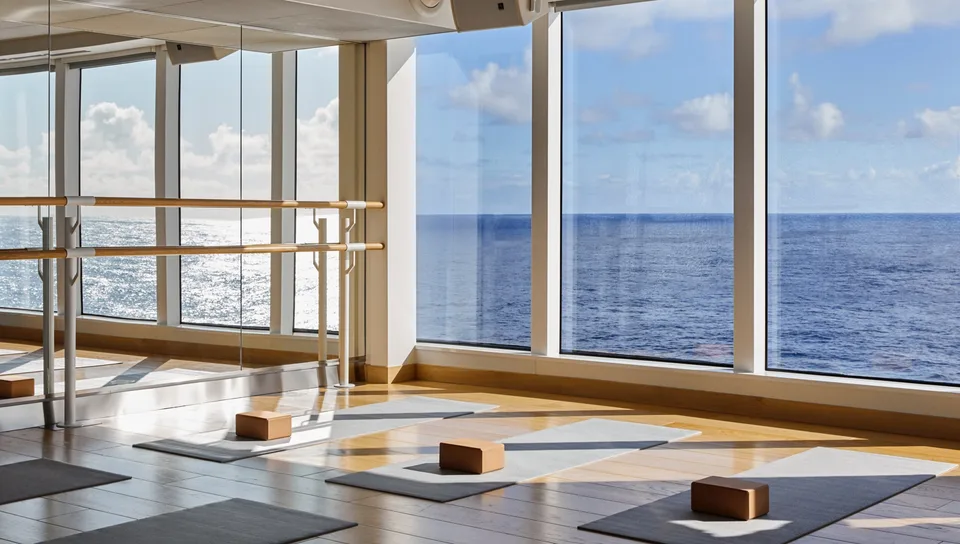 Interior view of a ship's onboard fitness area with yoga mats and blocks, featuring large windows overlooking the ocean.