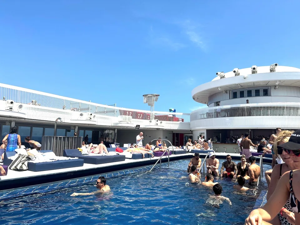 Passengers relax and swim on the deck of a cruise ship under a clear blue sky.