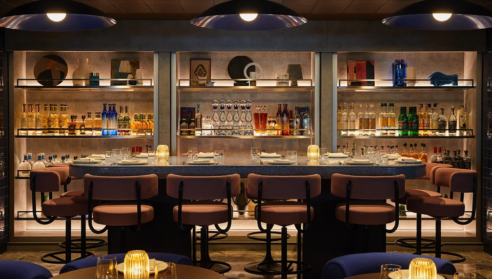 Onboard bar area with a row of padded bar stools, shelves stocked with bottles of liquor and water, and candle-lit tables.