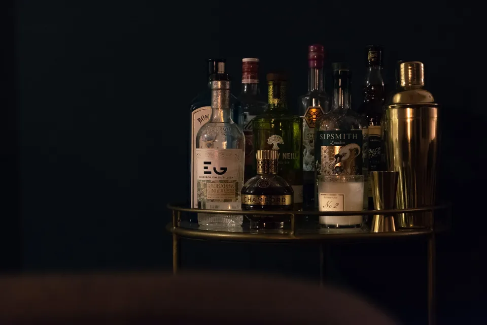 A variety of liquor bottles, including Sipsmith gin, arranged on a glass and metal shelf against a dark background.