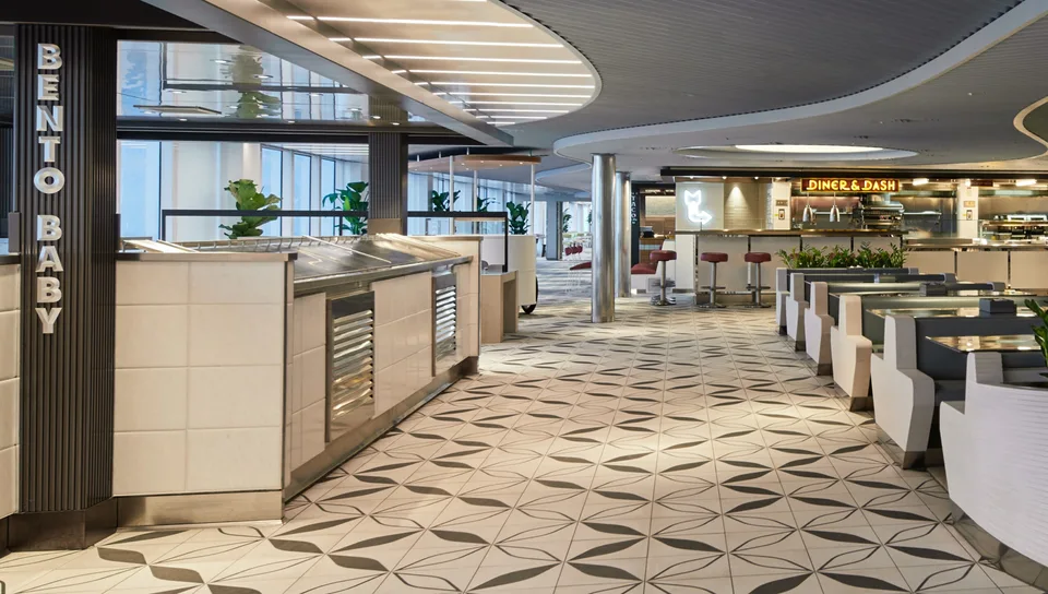 Onboard travel image showing a modern buffet counter labeled "Bento Baby" with a geometric patterned floor and large windows in the background.