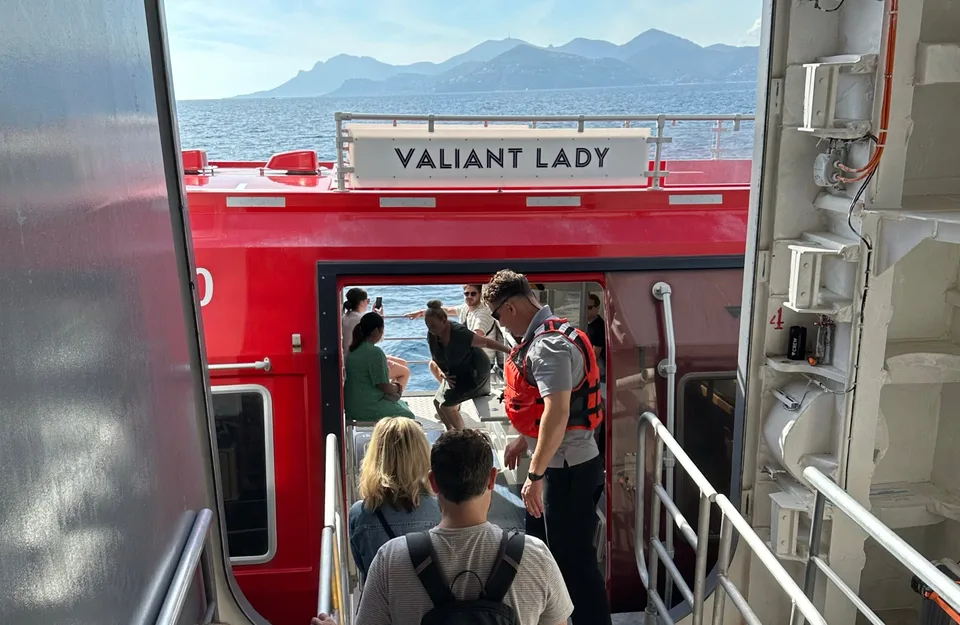 Passengers boarding or disembarking a red and white vessel named "Valiant Lady" with a crew member wearing a life jacket assisting.