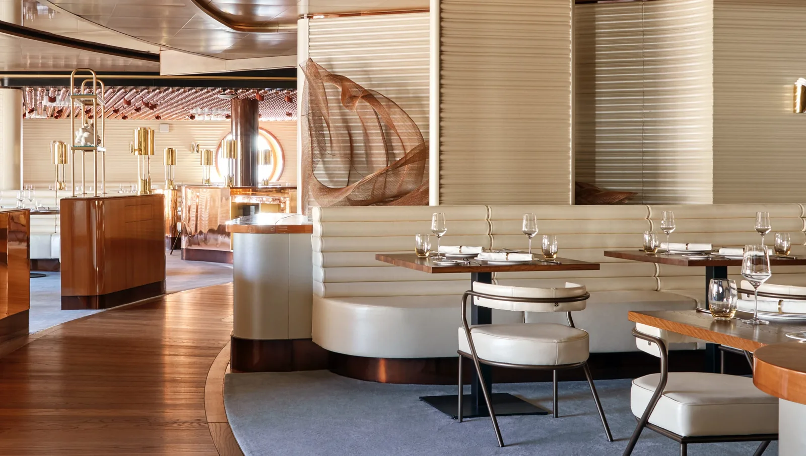 Interior view of a modern onboard dining area with wooden floors, white cushioned seating, and decorative elements including a saxophone and hanging glassware.