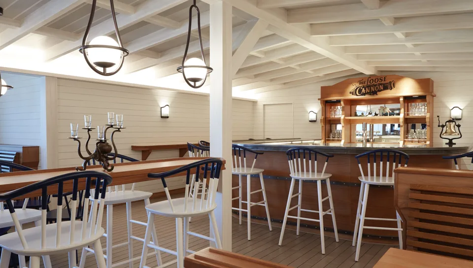 Interior view of a ship or boat lounge area with wooden chairs, tables, and hanging pendant lights.