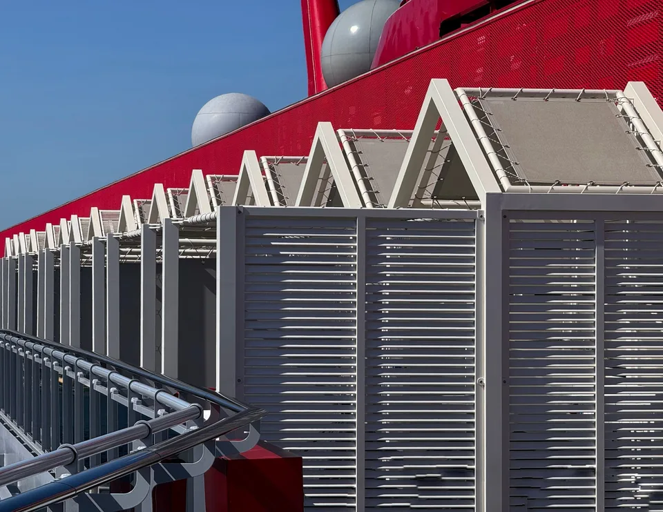 Close-up view of white louvered storage units or lockers on a ship deck with part of a red ship structure and blue sky in the background.