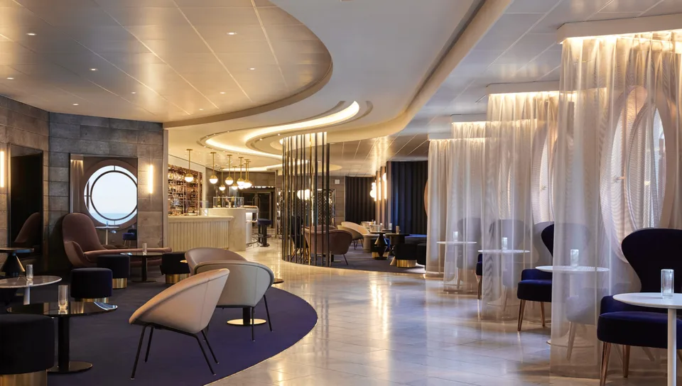 Modern, spacious onboard lounge area with contemporary seating, a bar, and large circular window.