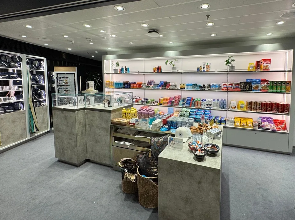 Onboard shop area displaying shelves stocked with snacks, drinks, and travel essentials, along with a counter and baskets.